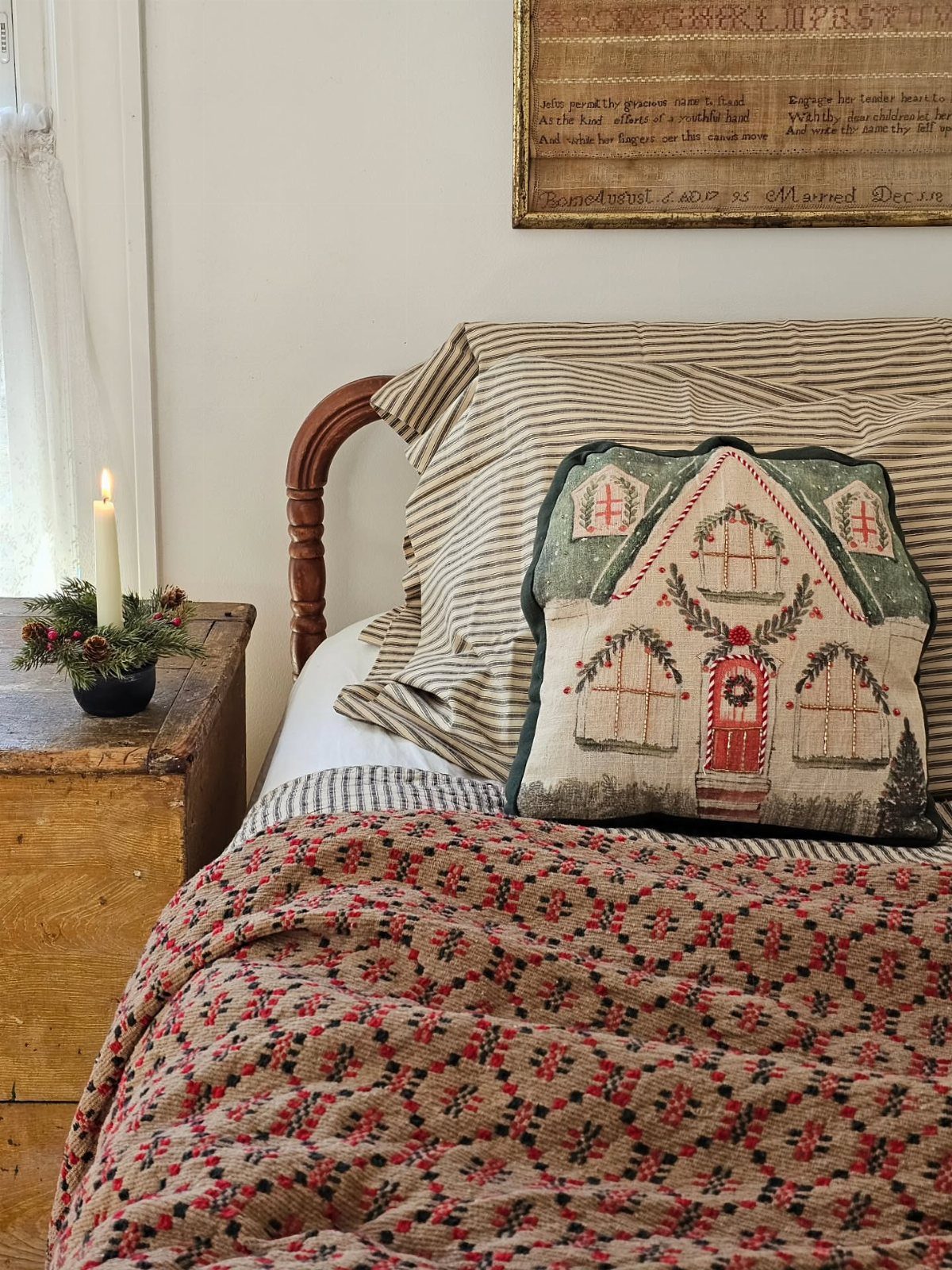 Bed with red patterned quilt and a house-themed Christmas decorative pillow.
