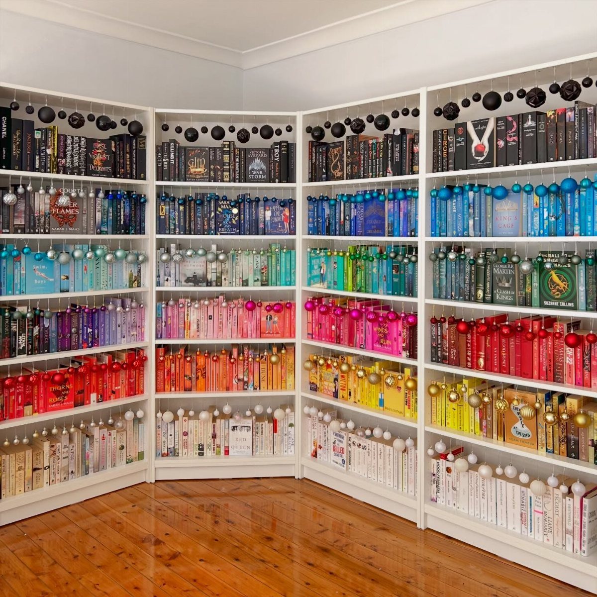 Rainbow colored books on white shelves decorated with hanging Christmas ornaments