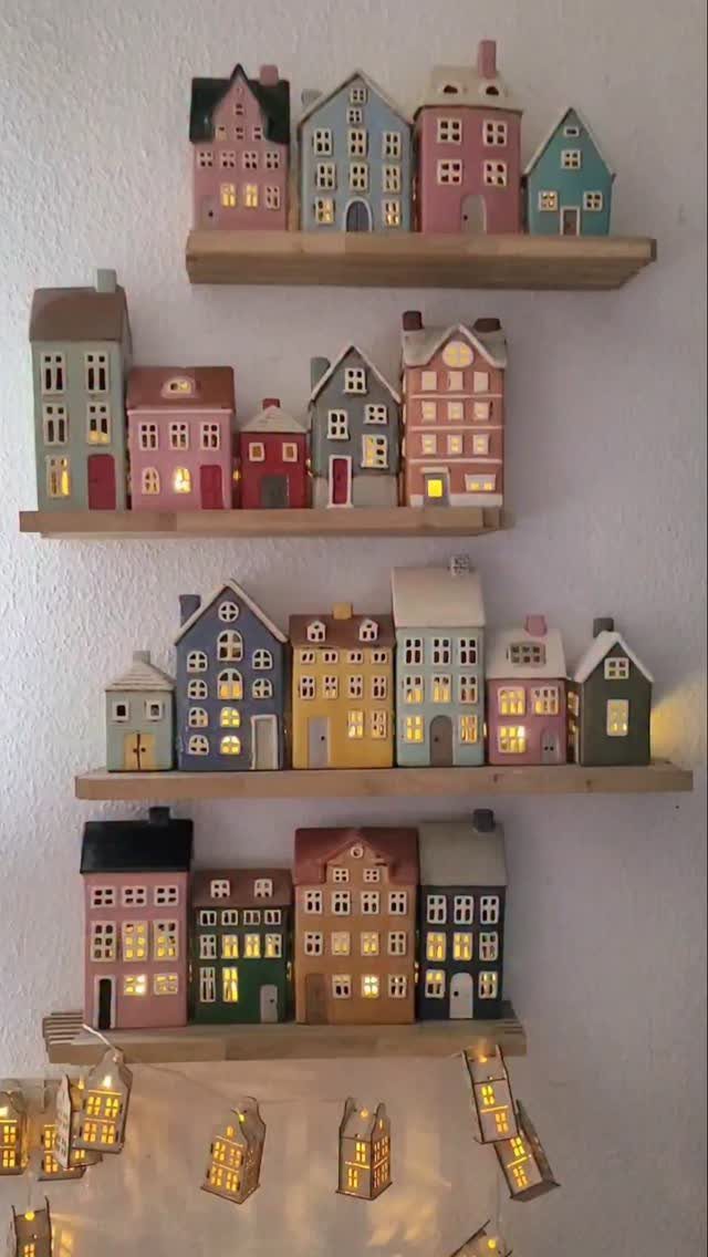 Colorful ceramic miniature houses with glowing windows displayed on wooden floating shelves.