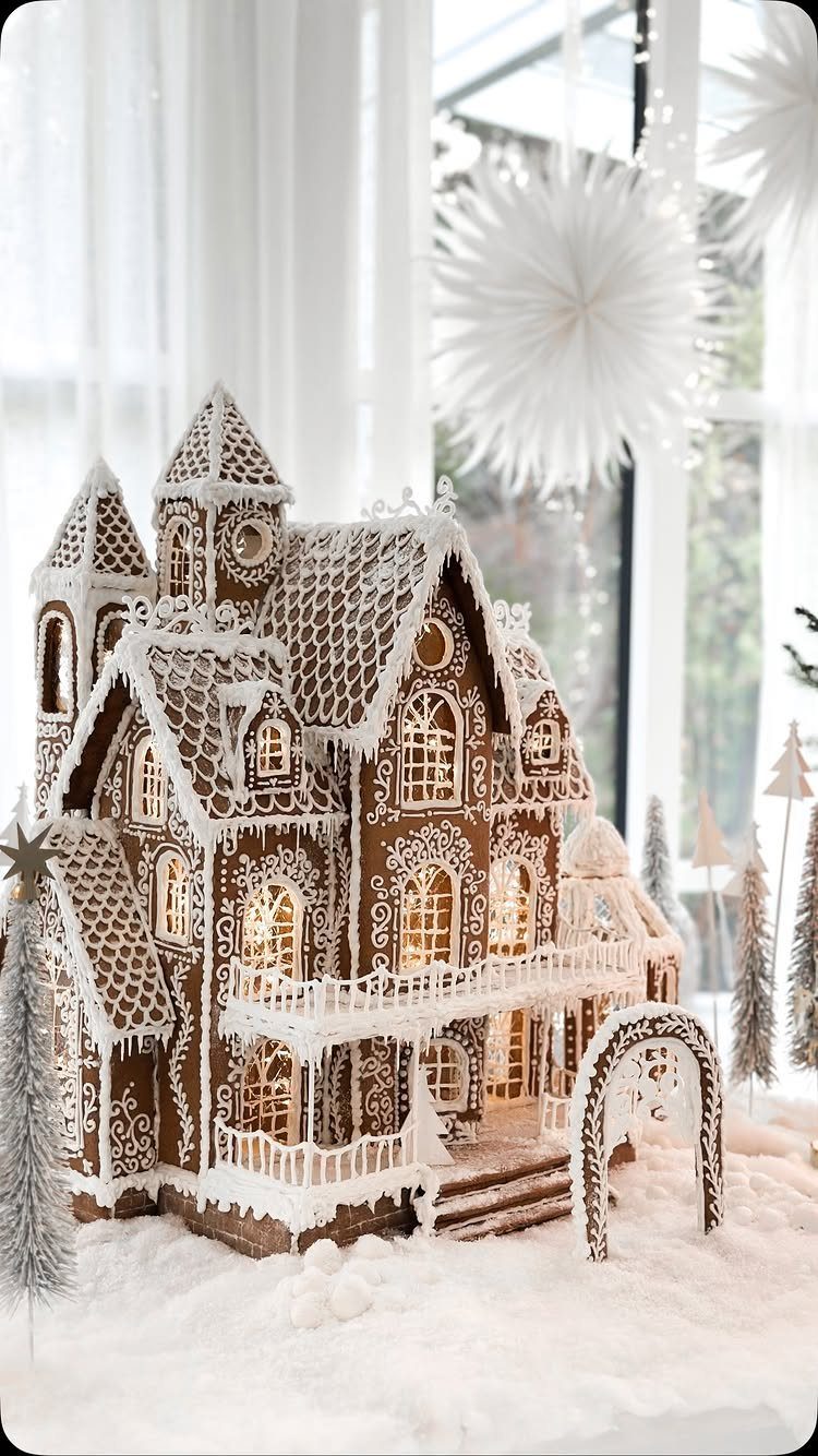 Intricate gingerbread house with white icing glowing from within on artificial snow.