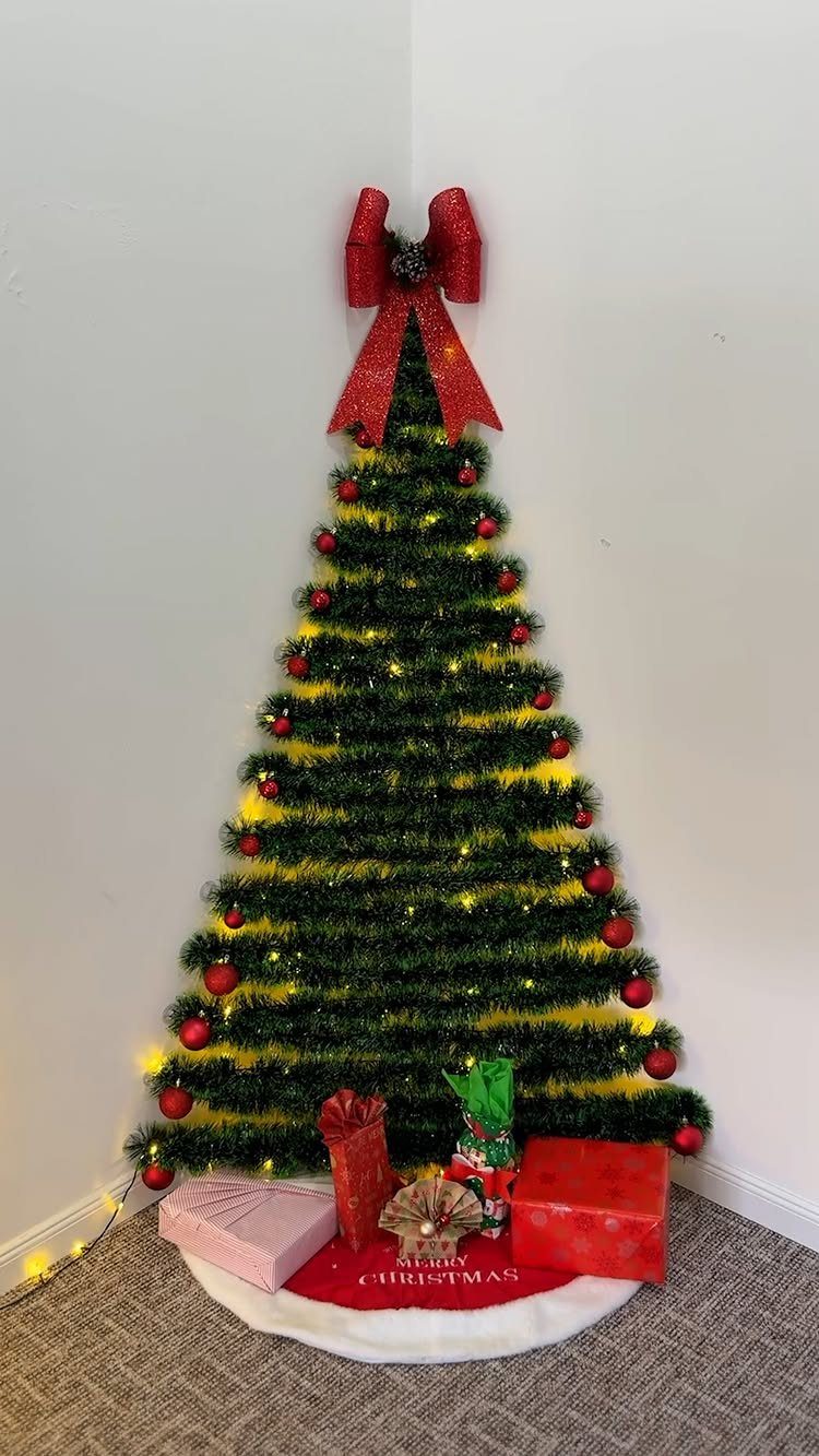 Tinsel garland Christmas tree on a wall with red ornaments and wrapped gifts.