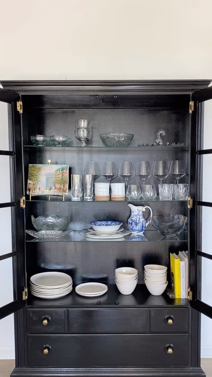 15 Small Living and Dining Room Ideas That Maximize Space 6 Black wooden kitchen hutch with open doors displaying glassware, white ceramics, and books.