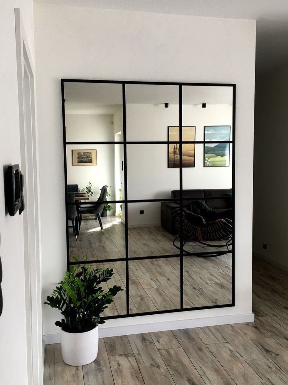15 Small Living and Dining Room Ideas That Maximize Space 10 Large black-framed window-pane mirror on a white wall reflecting a modern living room.
