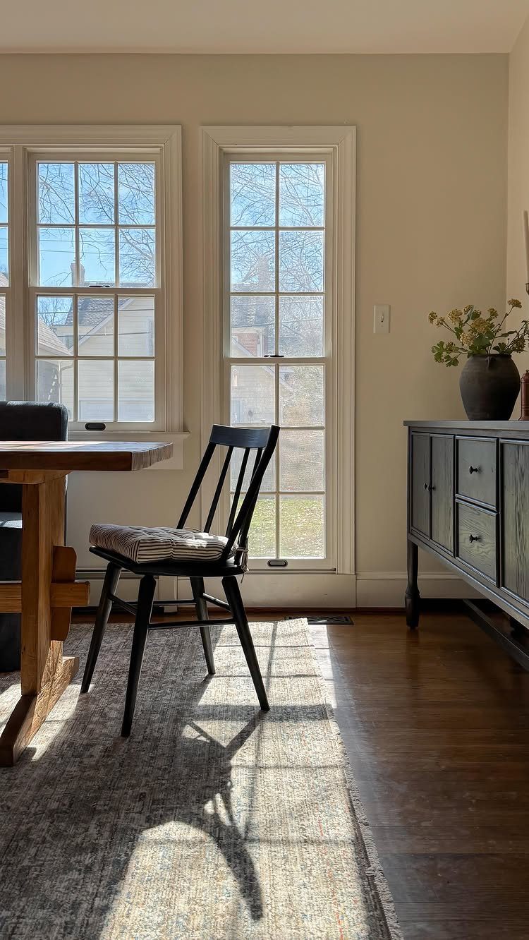 15 Small Living and Dining Room Ideas That Maximize Space 12 Wooden dining table and black chair placed beside bright white-framed windows in a room.