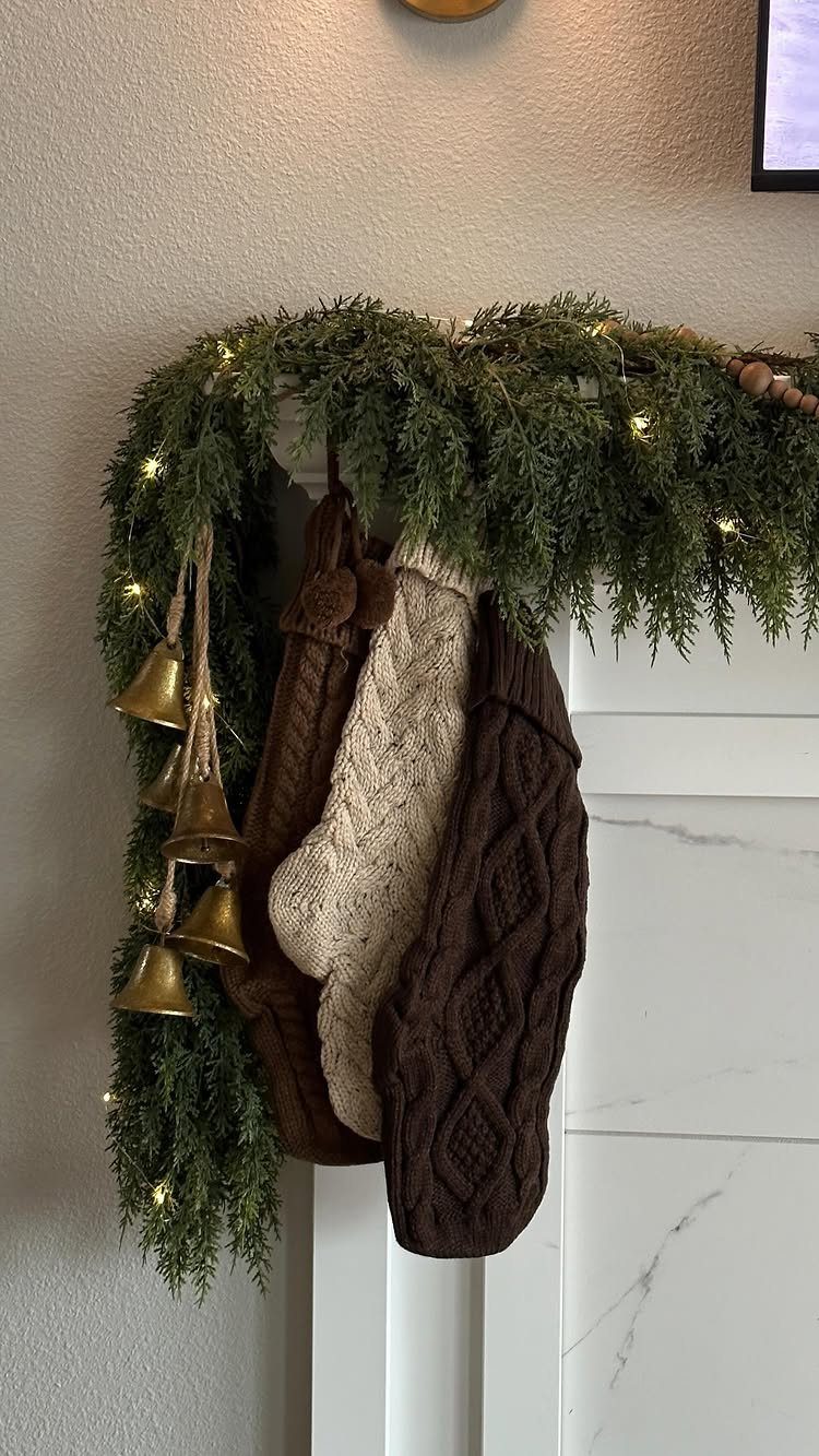 12 Studio Apartment Christmas Decor Ideas That Save Space 11 White fireplace mantel with green garland, gold bells, and knitted Christmas stockings.