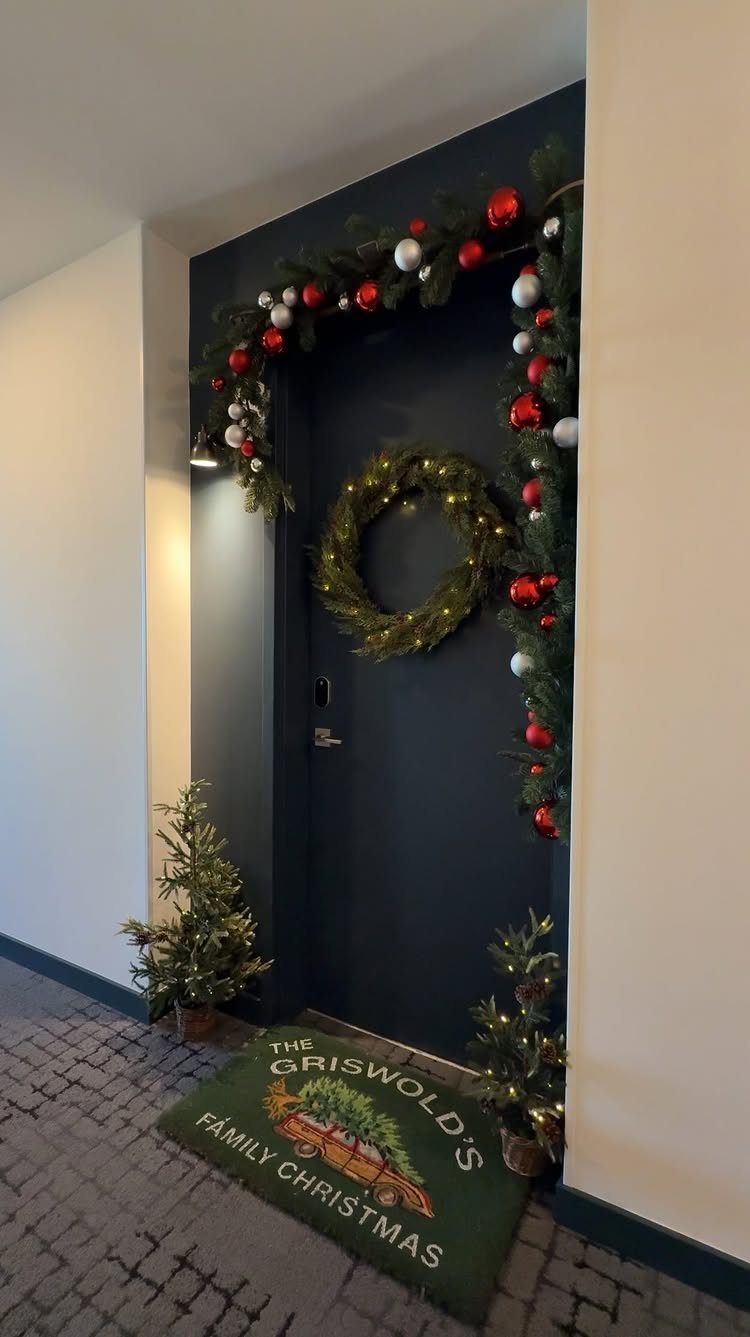 12 Studio Apartment Christmas Decor Ideas That Save Space 5 Dark blue door framed with festive pine garland, a wreath, and small potted trees.