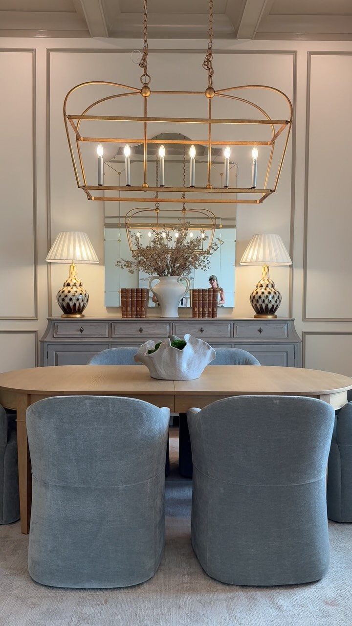 5 Transitional Dining Room Light Ideas for 2026 2 Gold transitional chandelier hanging over an oval wooden dining table with blue chairs.