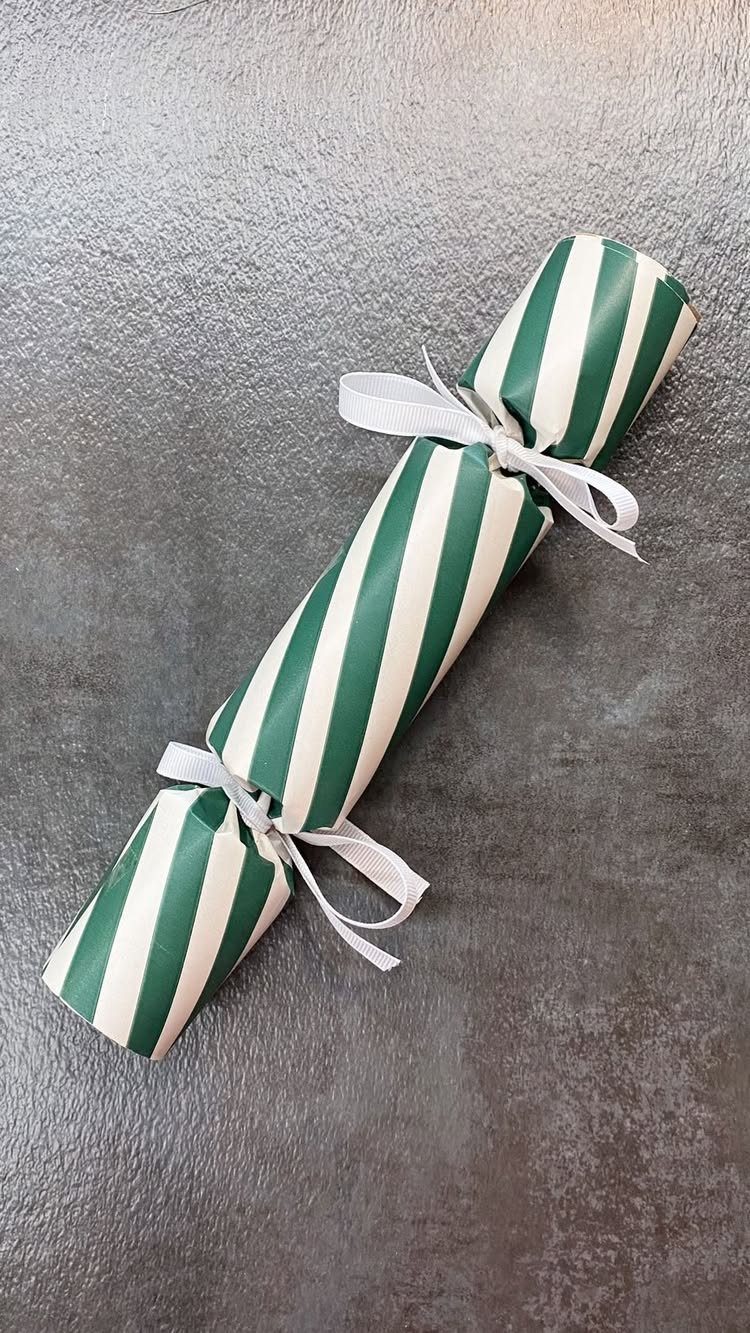 Christmas cracker with green and white stripes tied with white ribbons.