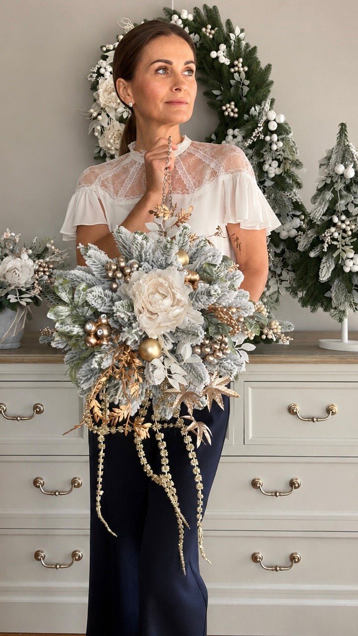 Woman holding a large, frosted kissing ball ornament with gold baubles and white flowers.