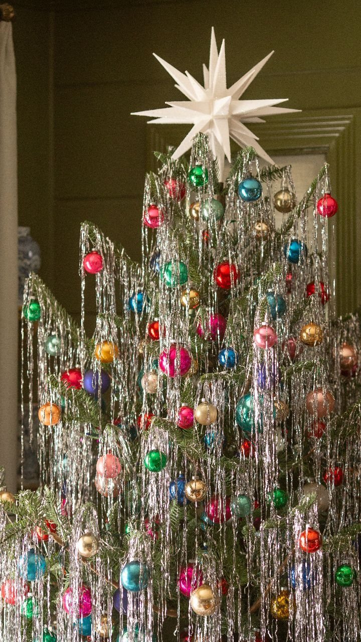 Christmas tree decorated with colorful ornaments and long silver tinsel strands under a star.