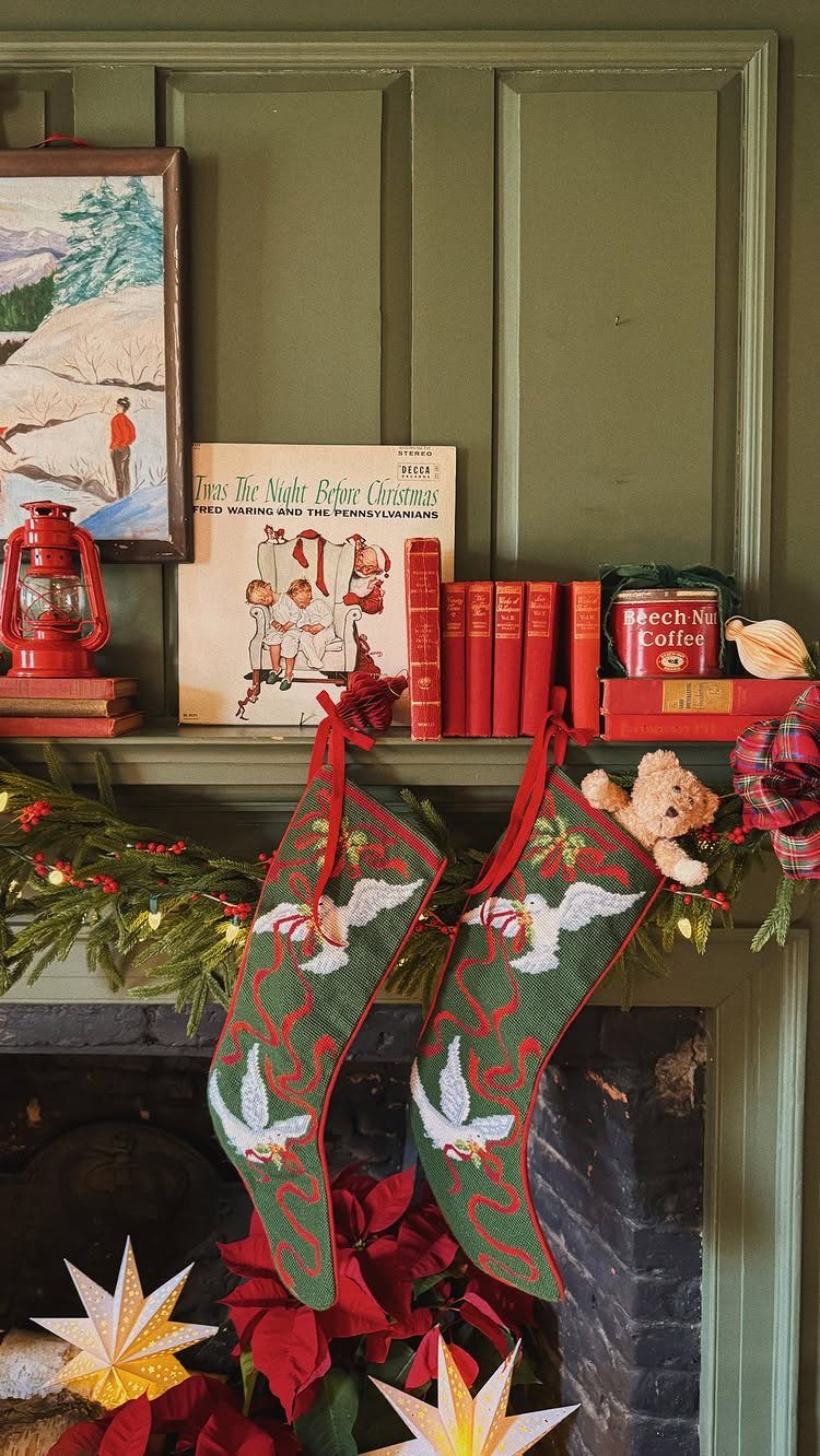 Vintage Christmas mantel with red stockings, old books, and a red lantern on green paneling.