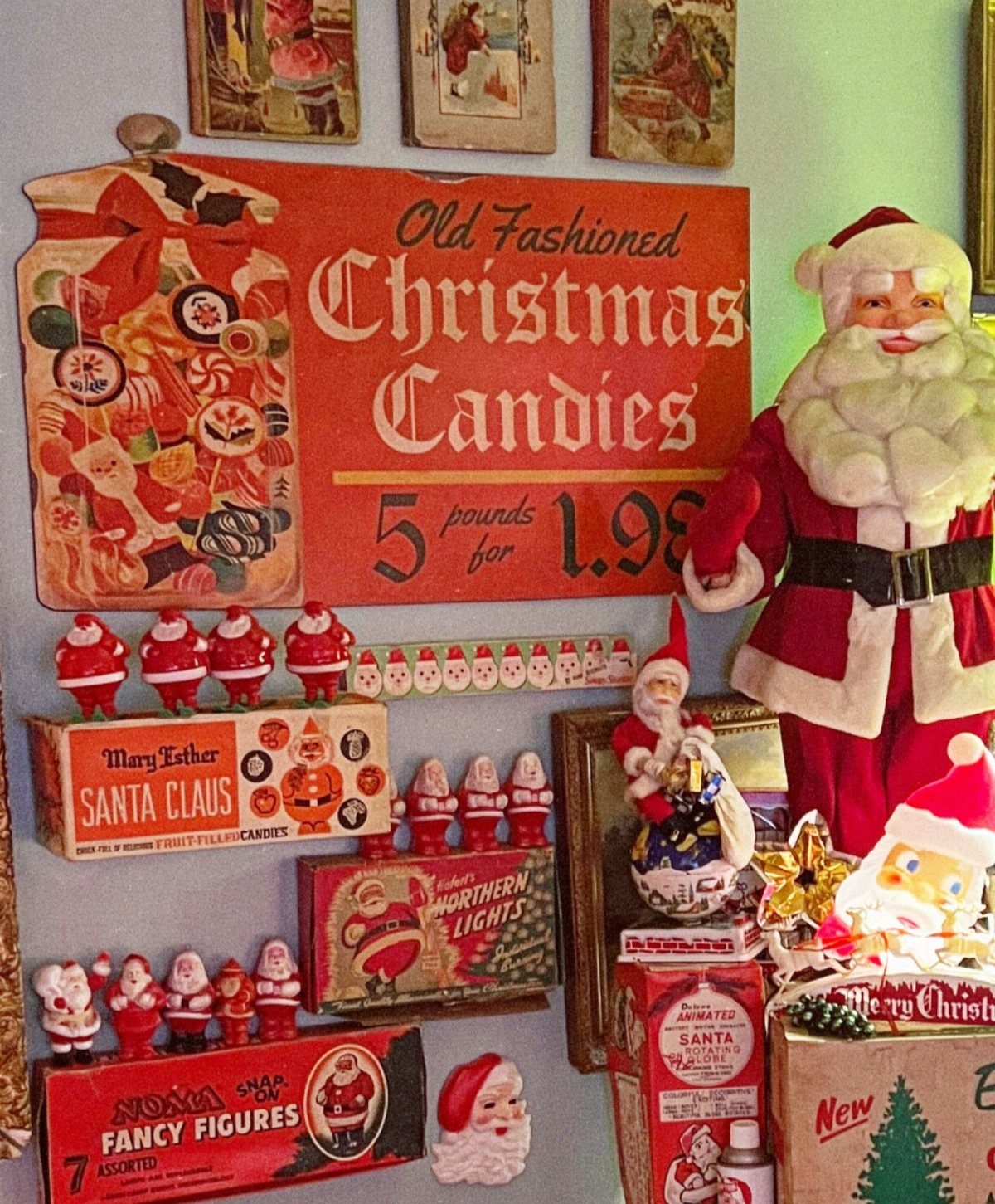 Vintage Christmas candies sign surrounded by Santa figurines and old holiday toy boxes.