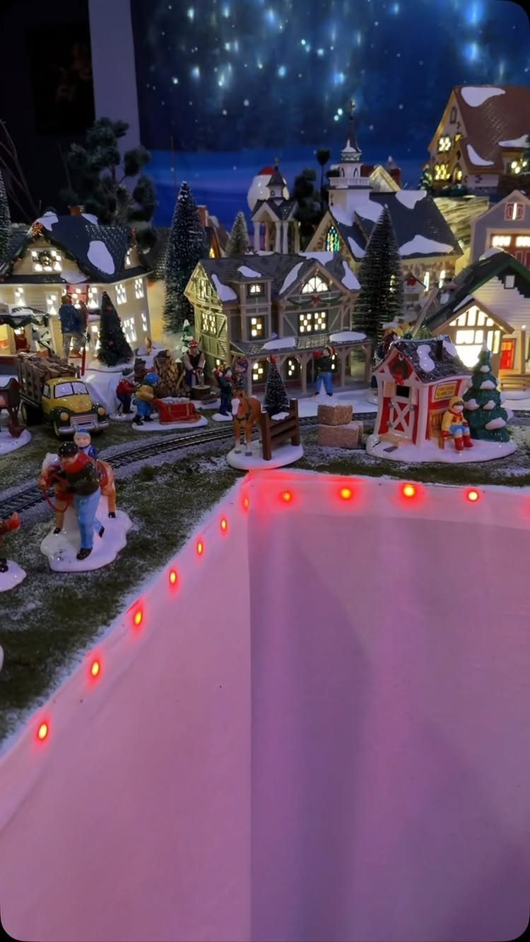Miniature Christmas village with snow-covered houses, figurines, and a starry night background.