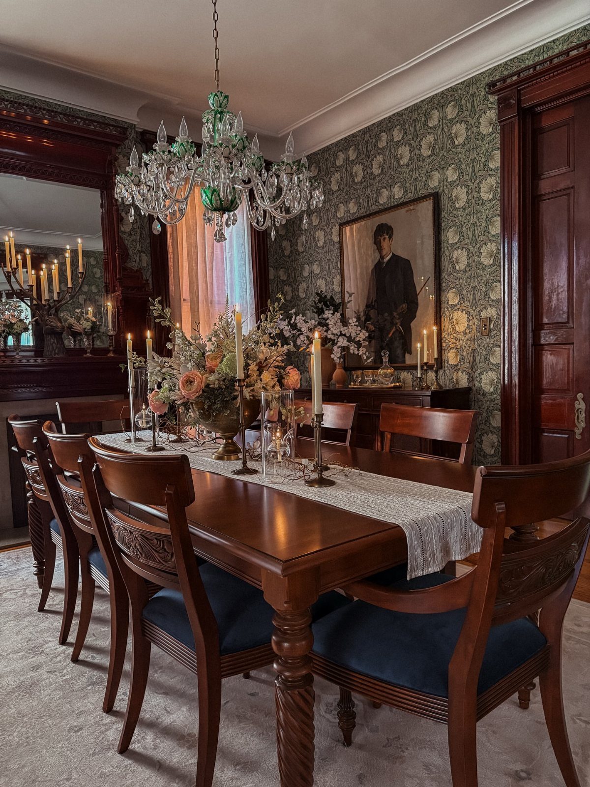 Formal dining room featuring a traditional framed portrait on patterned wallpaper with a chandelier.