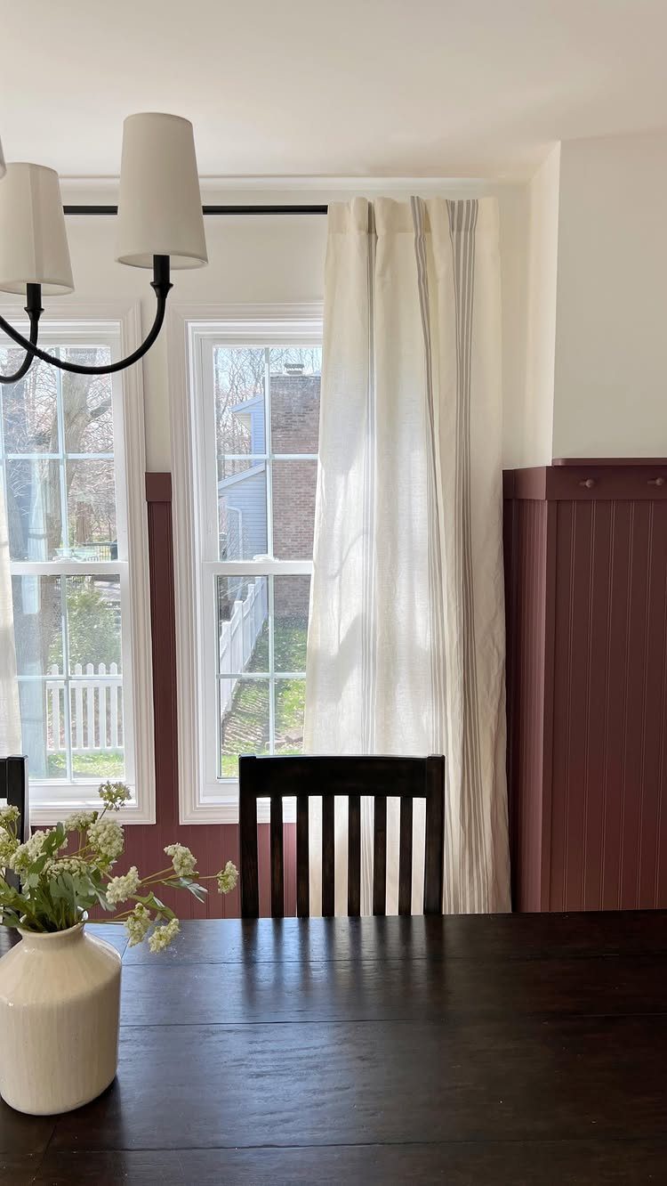 Dining room with reddish-brown beadboard paneling, dark wood table, and white curtains.