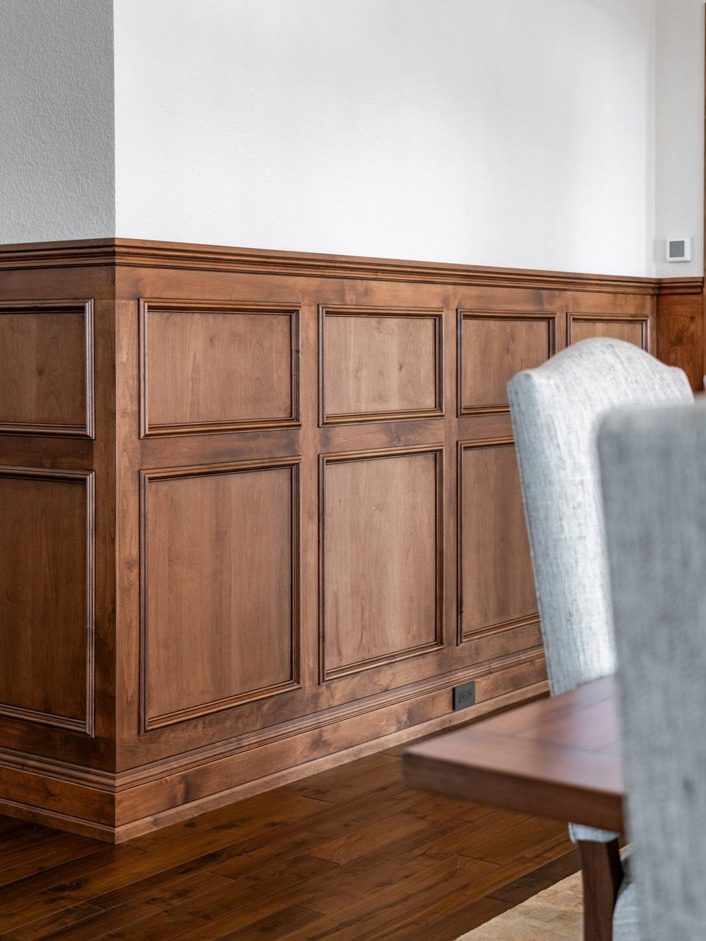 Brown wood wainscoting with raised panels in a dining room with grey chairs.