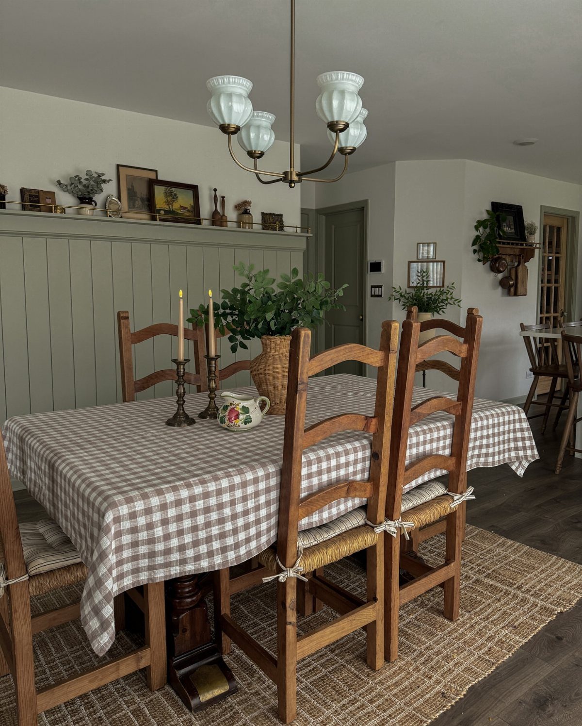 Wooden dining table with checkered cloth in a room with green wood paneling.