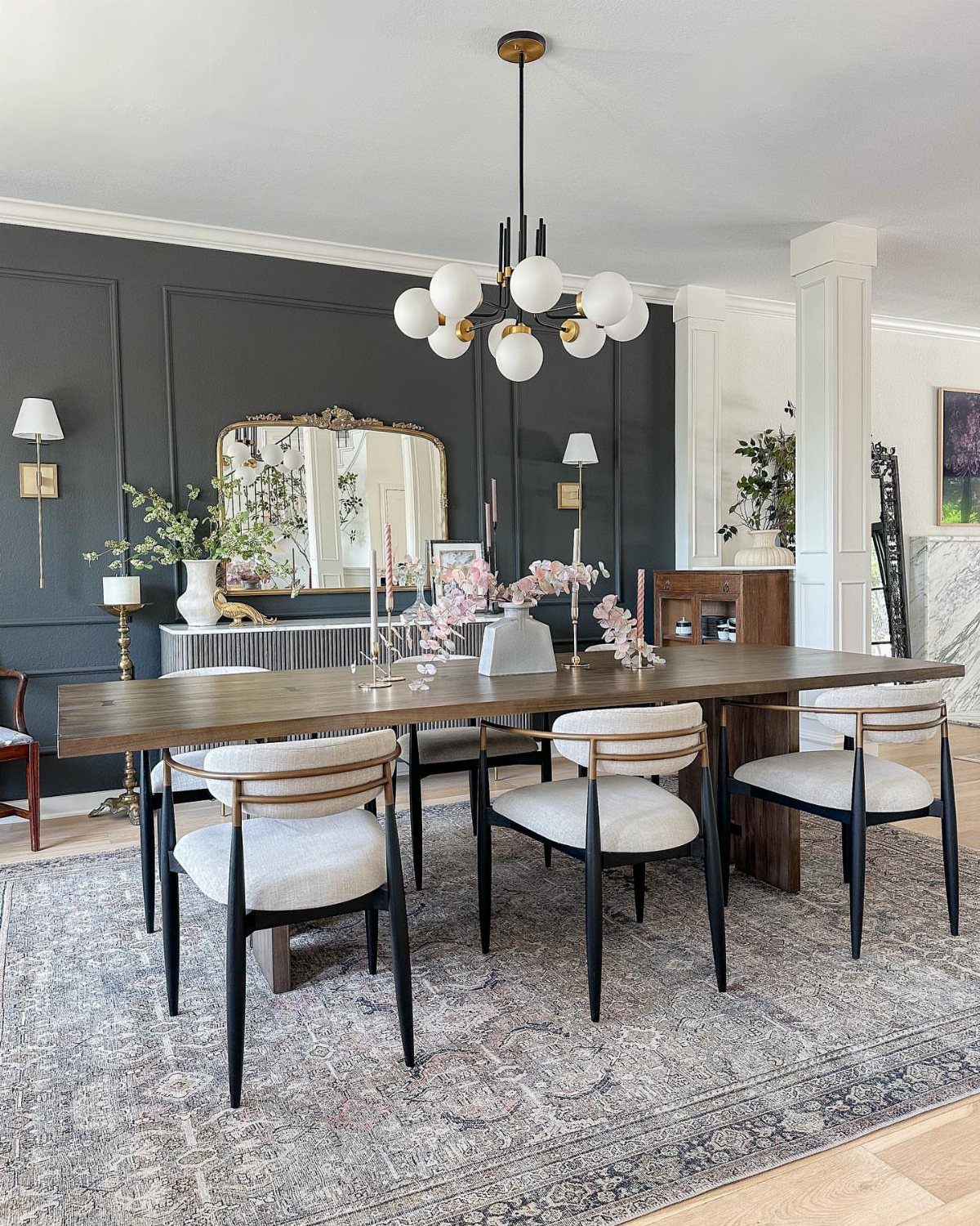 Dining room with dark grey raised panel walls, wooden table, and globe chandelier.