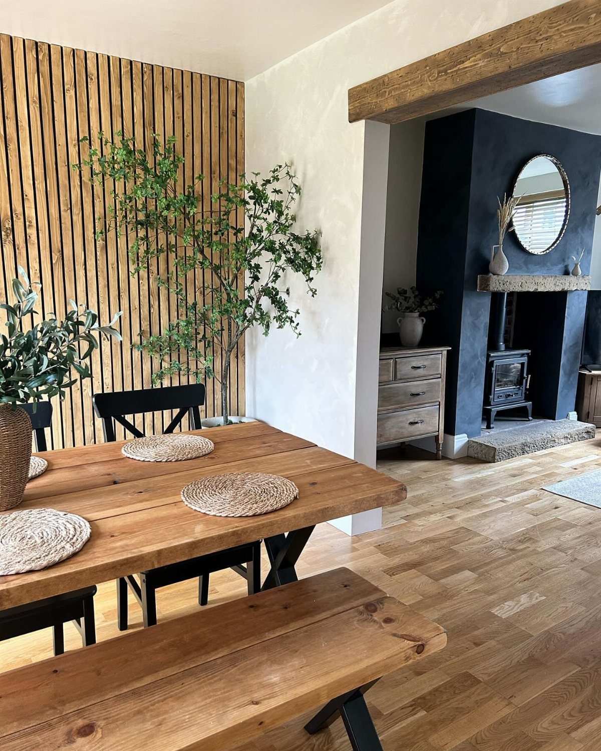 Wooden dining table and bench set against a vertical slatted wood wall.